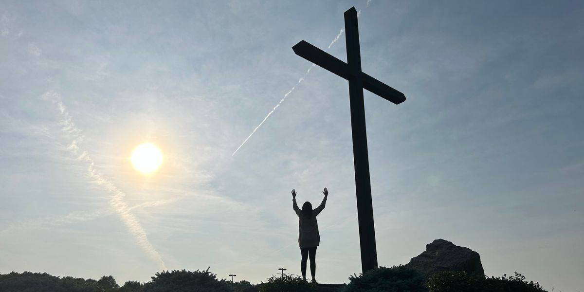 woman lifting hands in praise in front of a cross